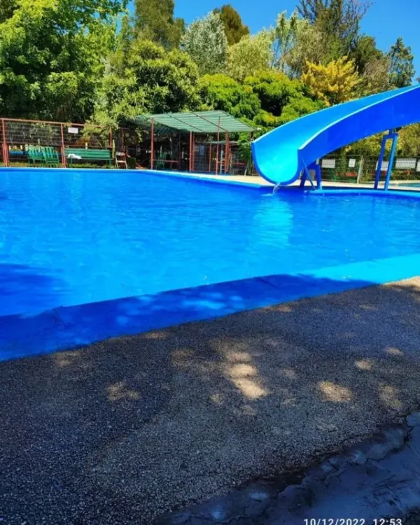 Piscina de agua azul con salida de tobogán y árboles al fondo